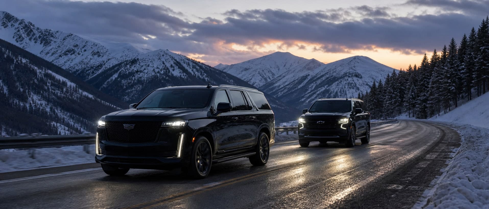 Two black executive SUVs in convoy on a snowy Colorado mountain highway at sunset.