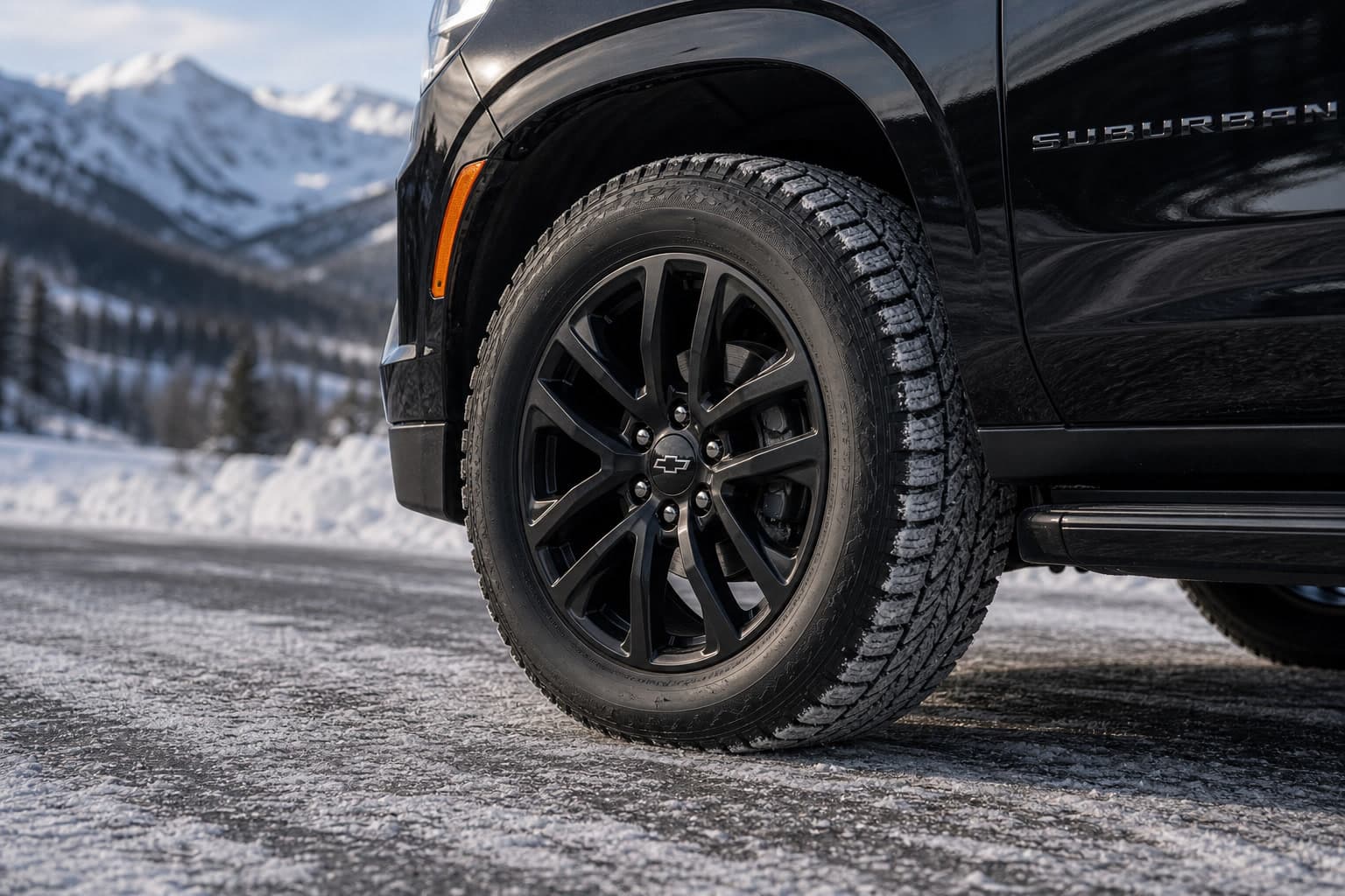 Close detail of a dedicated winter tire on a black Suburban with a snowy mountain pass in the background.