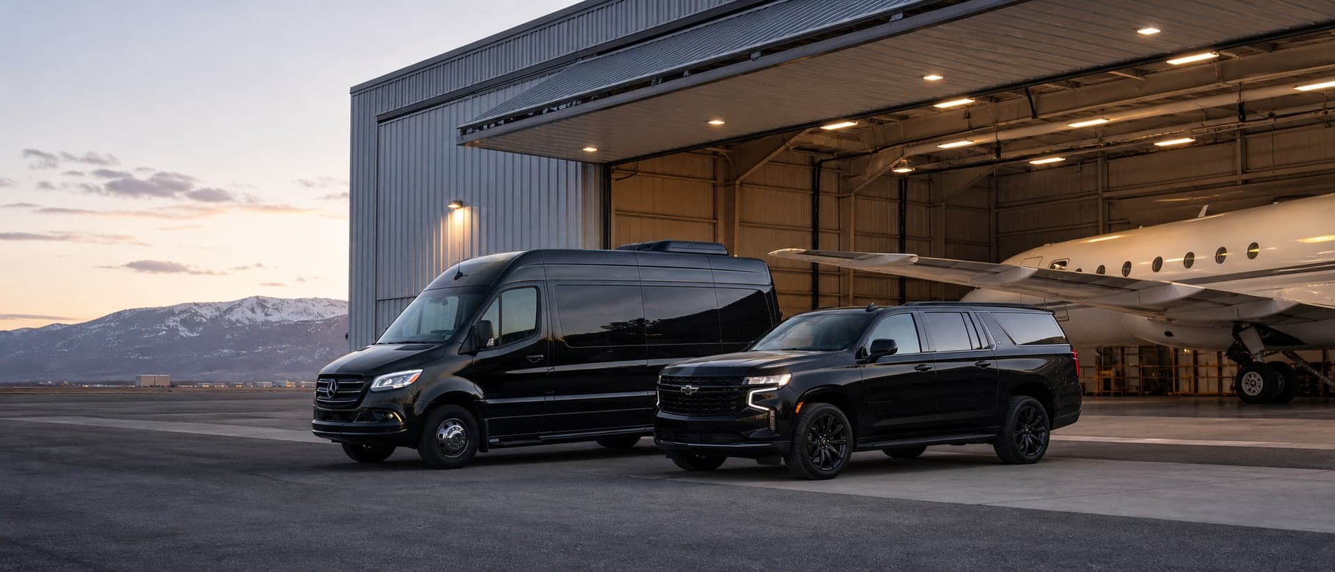 Black Sprinter and Suburban staged at a Colorado hangar near Snowmass at dusk.