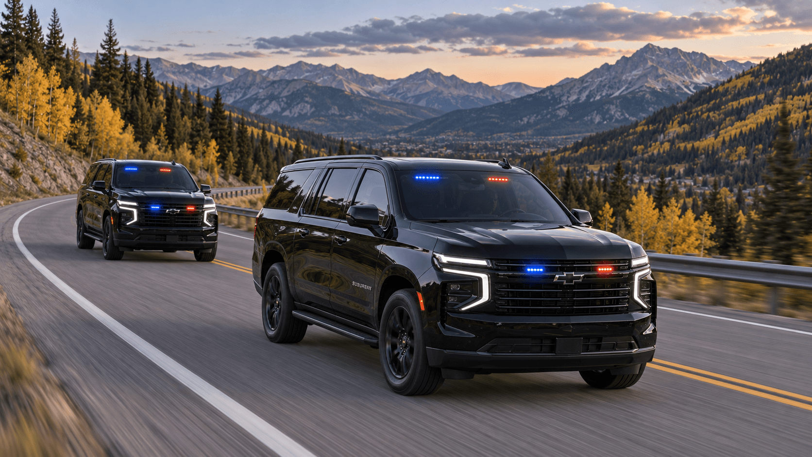 Two black SUVs with red and blue grille and windshield lights driving a mountain highway above a valley at sunset.